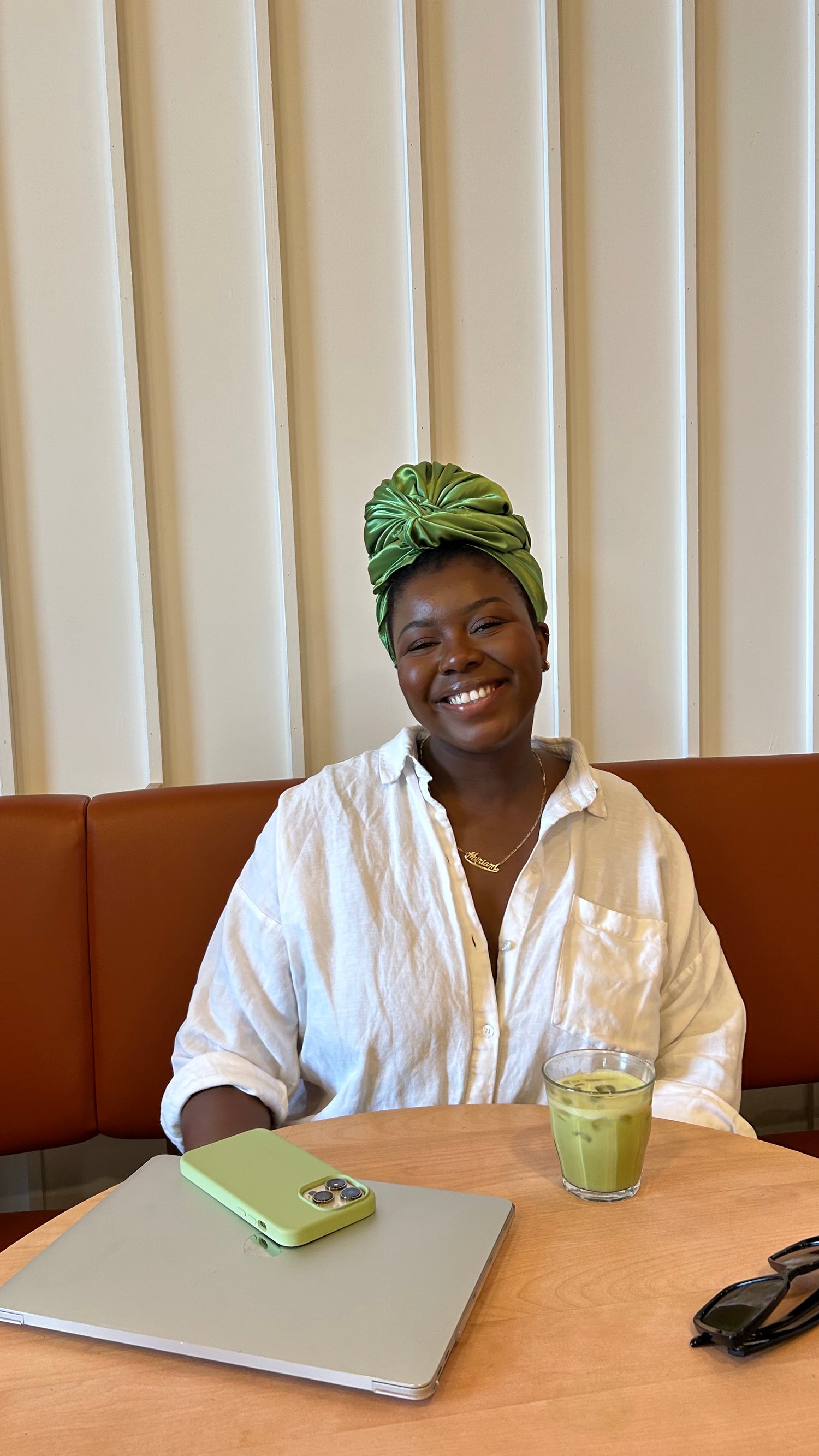 Dans cette image, nous voyons Miriam Nkosi, fondatrice d'imawrap qui porte un foulard en satin vert nommé Jolene. Elle est assise et sourit